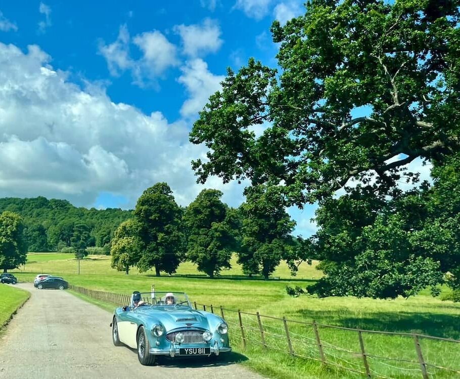 A blue convertible driving up a lane with fields either side