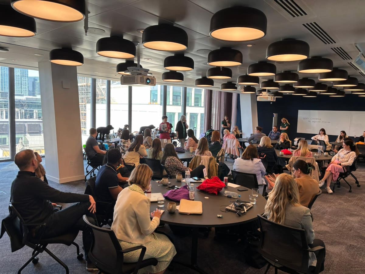 Groups in a room sat round several tables, with presenters at the front